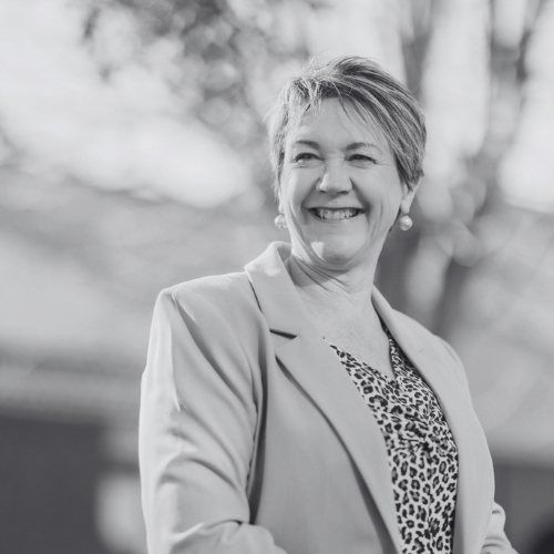 Smiling woman in a blazer standing outdoors, in black and white.