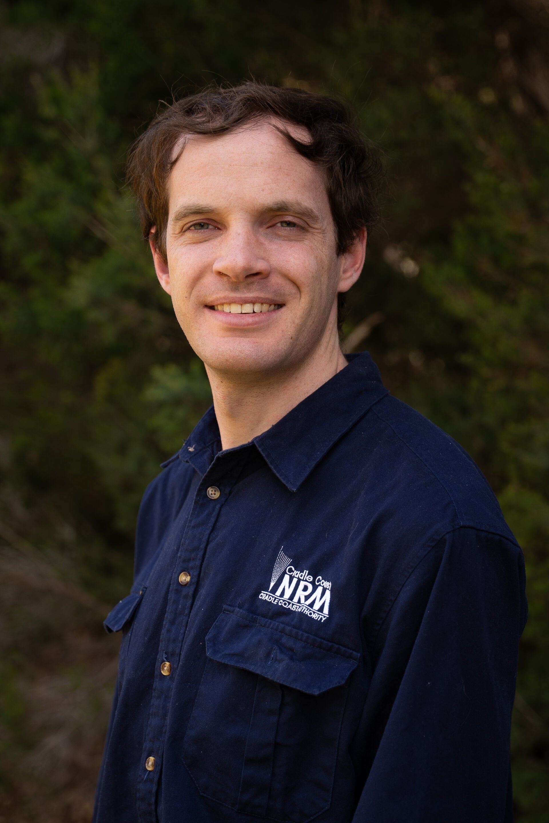 Man wearing a navy shirt with visible NPA logo, standing outdoors with greenery in the background.