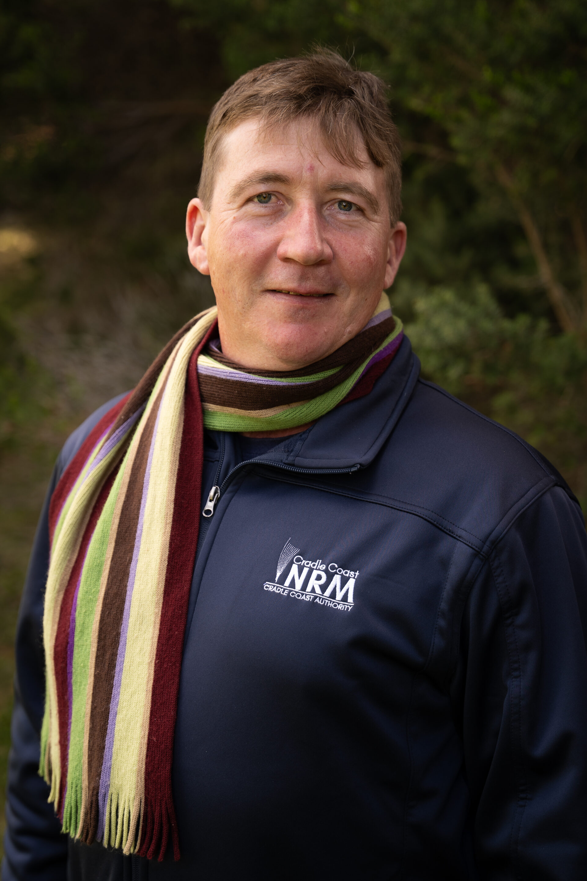 Person wearing a navy jacket and striped scarf standing outdoors, smiling at the camera.