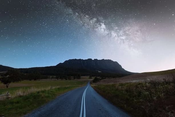 A road leads to a Mt Roland under a night sky with stars and the Milky Way visible.