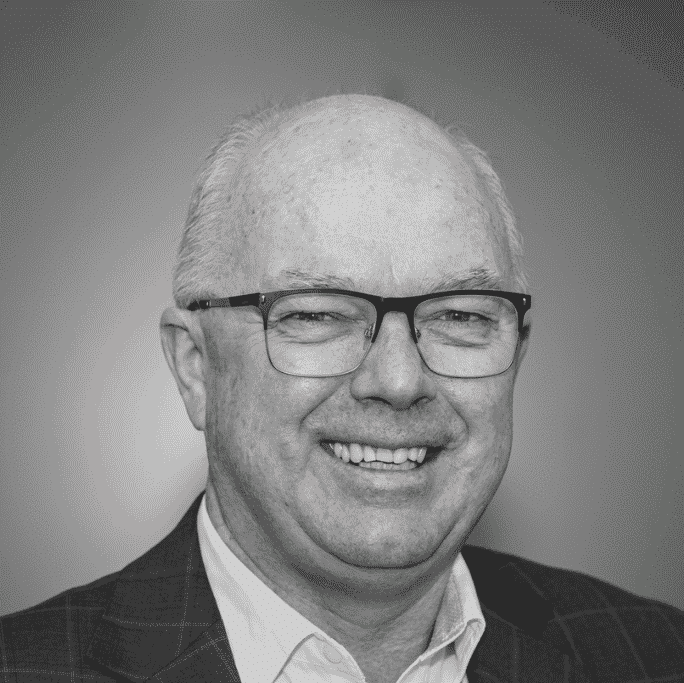 Older man with glasses, short white hair, and a suit jacket, smiling at the camera against a plain background.