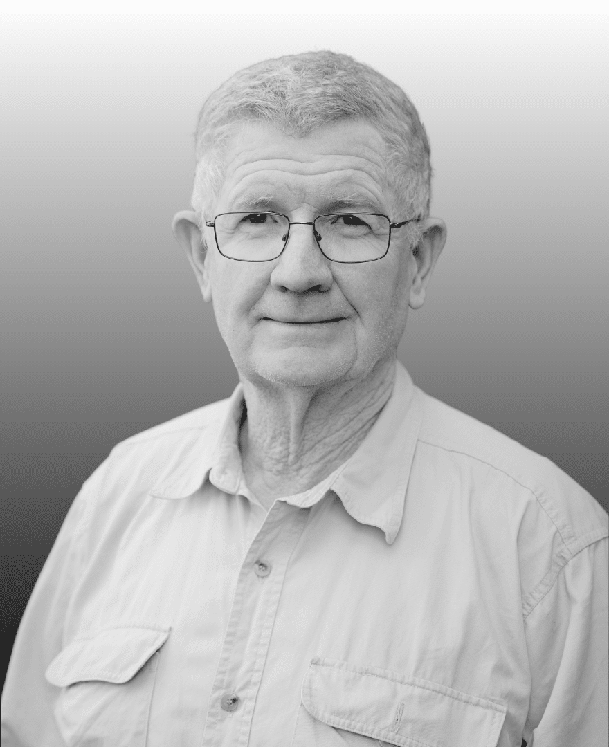 Older man with short grey hair, spectacles, and a light-coloured button-up shirt facing forward against a gradient background.